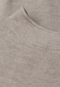 Vahva beige neulekangas, jossa on rytmikäs pinta, sujuva kaula-aukko ja hienovarainen langan vaihtelu. Näyttää materiaalin kudontatarkkuuden.