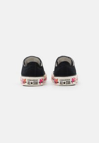 Zapatillas bajas de lona negras con una suela de goma impresa colorida que lleva la marca "Converse All Star", costuras visibles y un tejido texturizado.