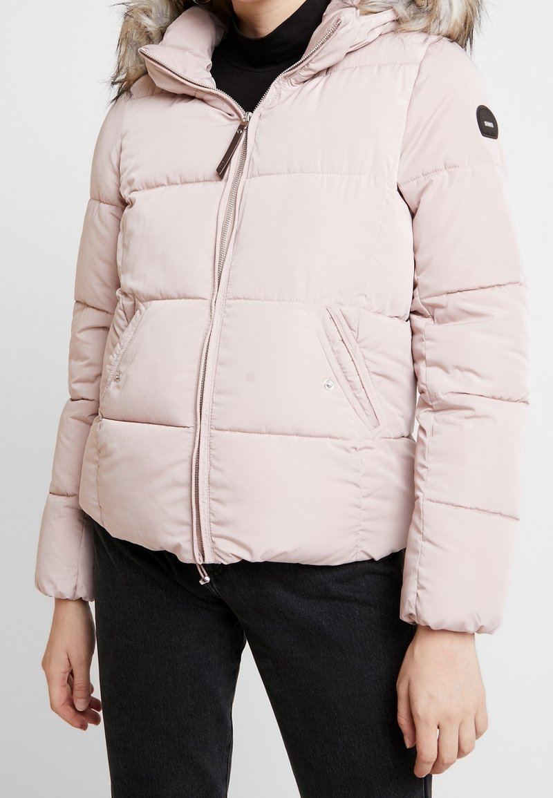 Světle růžová prošívaná bunda s kapucí lemovanou umělým kožíškem, zapínáním na zip a bočními kapsami. Prošívaný design přidává texturu a teplo.