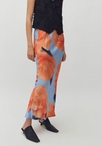 Vloeiende maxi-jurk in lichtblauw, met grote oranje bloemenpatronen. Gekocht met een zwarte textuurvest en zwarte muiltjes.