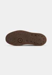 Semelle en caoutchouc marron avec des motifs de bande de roulement circulaires et ondulés, des trous de ventilation et un petit logo embossé près du talon.