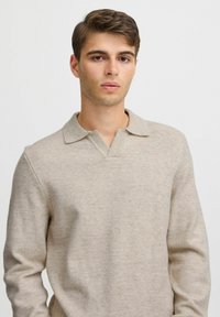 Beige kötött pulóver, galléros nyakkal és textúrált felülettel, hosszú ujjakkal és laza szabással. Egyszerű, minimalista dizájn.