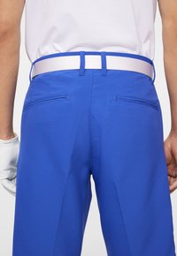 Niebieskie spodnie golfowe o teksturowanym wykończeniu, z dwoma tylnymi kieszeniami, białym paskiem oraz czystymi, dopasowanymi liniami.