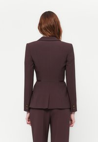 Bordeaux takoitettu bleiseri, jossa on muotoillut olkapäät, peplum-muotoilu ja kultaiset napin yksityiskohdat. Sileä kangas hienolla viimeistelyllä.