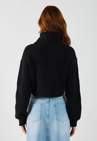 Maglione nero lavorato a maglia con colletto alto e texture a coste, abbinato a una gonna in denim azzurra con tasche sul retro.