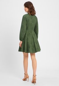 Green, knee-length dress with flared skirt, long sleeves, and eyelet design. Paired with tan high-heeled sandals. Back view displayed.