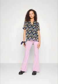 Camisa com estampado floral em azul marinho com flores amarelas e brancas; combinada com calças flare rosa claro e sapatos de plataforma pretos. Inclui uma faixa em azul marinho para o pulso.