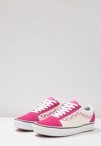 Vaaleanpunaiset ja kermaiset tennarit, joissa on ruutukuviota, valkoiset nauhat, kumipohja ja sileä kangaspinta.