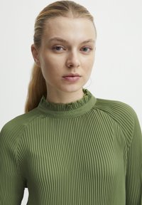 Top verde a maniche lunghe con collo alto arricciato e motivo texturizzato, caratterizzato da una silhouette aderente e un tessuto liscio.