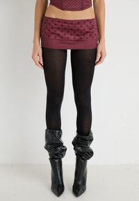 Jupe mini rouge à pois, avec une texture lisse, associée à des collants opaques noirs et des bottines en cuir noir, souples, à bout pointu.