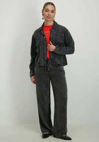 Veste en denim foncé avec deux poches avant, associée à un pantalon en denim foncé ample et un t-shirt rouge. Des chaussures noires à talons pointus complètent l'ensemble.