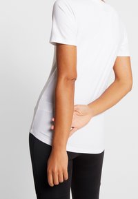 Hvid kortærmet t-shirt lavet af letvægtsstof, med rund halsudskæring og en glat tekstur, parret med sorte leggings.