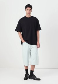 Tricou scurt negru cu mânecă scurtă, pantaloni scurți din denim bleu deschis, și pantofi de dress negri. Croi simplu și fit relaxat; culori uni fără modele.