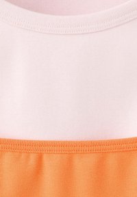 Gros plan d'une couture de tissu joignant des sections tricotées en coton rose clair et orange avec des points visibles à la jonction.