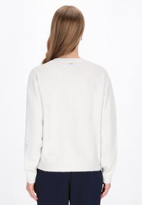 Pull en tricot blanc avec un col rond, texture douce, poignets et ourlet côtelés, présentant de petites éclaboussures de couleur dans tout le tissu.