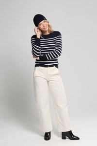 Maglione a strisce blu navy e bianche, pantaloni ampi color crema, stivaletti neri con tacco e un berretto blu navy. Outfit semplice e casual.