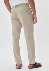 Beige byxor med rak passform, elastisk midja, två bakfickor och ett lätt, strukturerat tyg. Bärs med bruna sandaler.
