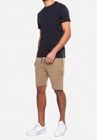 T-shirt noir à manches courtes associé à un short beige côtelé. Des baskets blanches complètent le look. Le short est muni de poches latérales et d'un cordon de serrage.