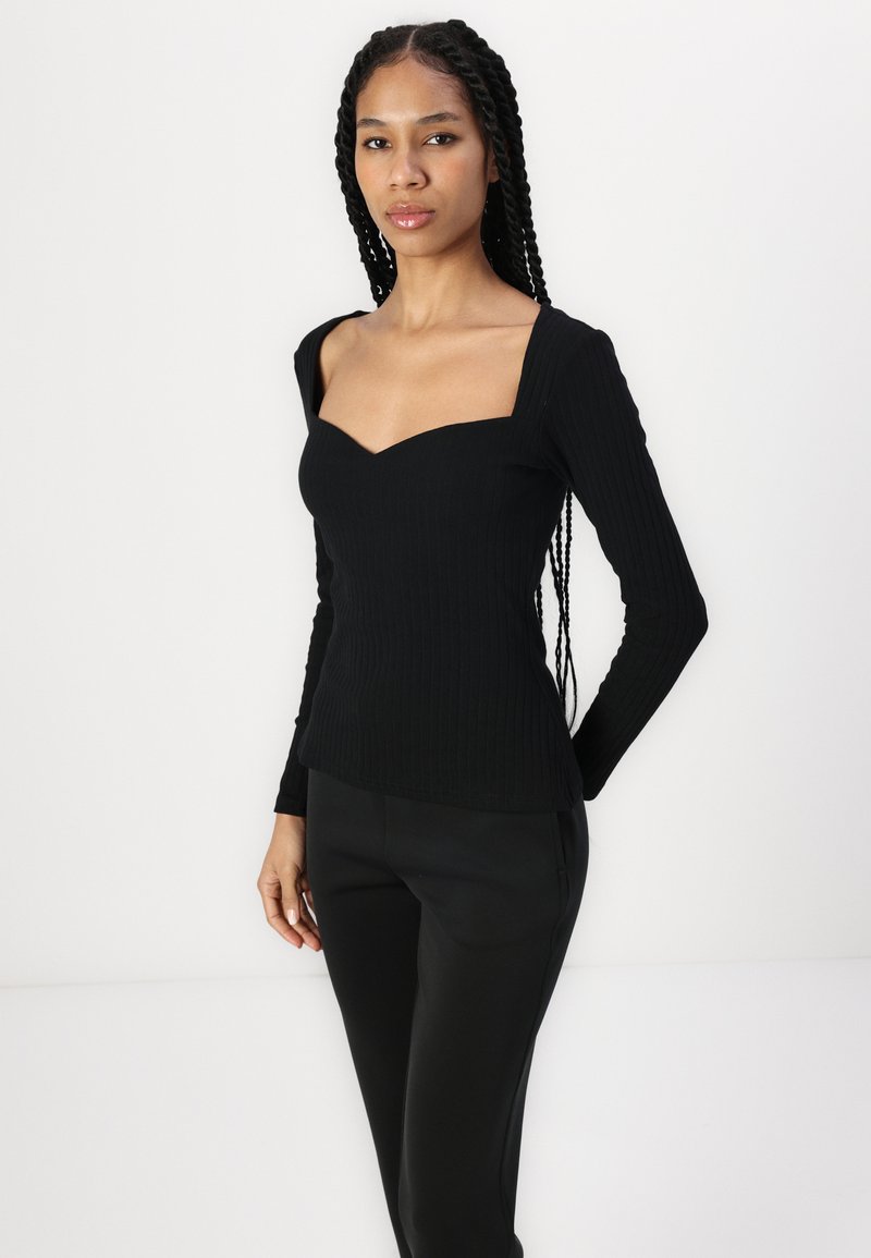 Czarny, żeberkowy top z długim rękawem, o szerokim kwadratowym dekolcie i dopasowanym kroju, zestawiony z czarnymi spodniami, prezentowany na białym tle.