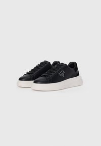 Black leather sneakers with a smooth texture, white rubber sole, and lace-up design. Features a logo on the side and a rounded toe.