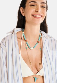 Collana a più fili con perle di turchese, catena dorata e una grande perla. Accenti sottili e vivaci migliorano il design complessivo e il contrasto dei colori.