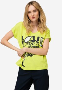 Camiseta de corte V de color amarillo neón hecha de tela suave, con un estampado gráfico que presenta la palabra "AMOR" y un dibujo de línea negra. Mangas cortas y corte suelto.