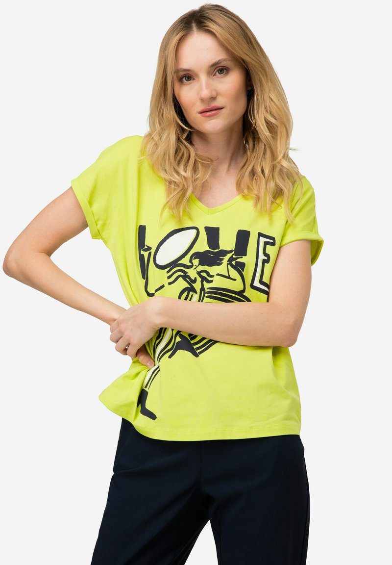 Camiseta de corte V de color amarillo neón hecha de tela suave, con un estampado gráfico que presenta la palabra "AMOR" y un dibujo de línea negra. Mangas cortas y corte suelto.