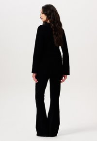Ensemble en velours noir comprenant un haut ajusté à manches longues et un pantalon évasé, mettant en avant une texture lisse et un design élégant.