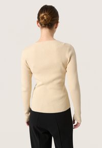 Ribbat långärmad topp i en ljusbeige färg, med en figurnära design, rundad halsringning och en något böjd fåll.