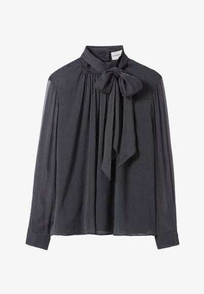 Blusa negra de manga larga con lunares blancos, cuello alto y un gran lazo atado en el escote.