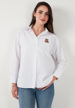 White long-sleeve button-up shirt, with an embroidered bear design on the left chest. Soft fabric, tailored collar, and straight cut.
