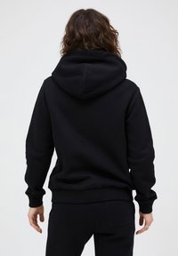 Zwarte hoodie van zacht materiaal, met een grote capuchon, ribgebreide manchetten en zoom, met een relaxed fit en zonder zichtbare logo's.