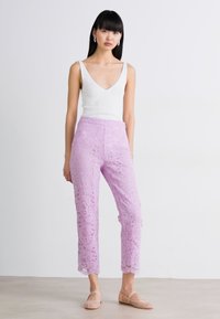 Lila kanten broek met een slim fit en cropped lengte, gecombineerd met een witte ribbel tanktop. Schoenen zijn beige met een zachte textuur.
