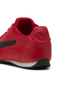 Scarpa sportiva rossa con tomaia in pelle liscia, striscia laterale nera, tallone testurizzato e suola in gomma bianca. Presenta piccoli fori di ventilazione.