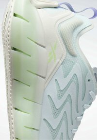 Chaussure de sport bleu clair avec semelle épaisse et translucide, motifs en mesh ondulés, lacets blancs et marquage vert clair sur le côté.