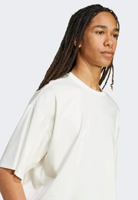 Šviesiai kreminė oversize marškinėliai su apvaliu kaklu, trumpomis rankovėmis ir lygiu paviršiumi, pasižymintys laisvu siluetu ir be matomų raštų.