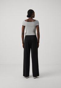 Grå off-shoulder ribbestrikket topp parret med svarte vide bukser, med en glatt tekstur og en skreddersydd passform. Synlige baklommer og hæler.
