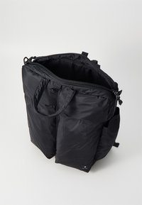 Sac fourre-tout noir en nylon avec une ouverture zippée, deux poignées et une surface texturée. Présente des poches latérales et un design minimaliste.