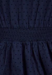 Sötétkék ruha texturált, függőleges csíkokkal és kis pöttyökkel, smockolt derékkal a nagyobb rugalmasság és térfogat érdekében.