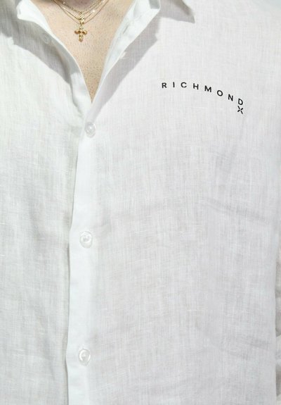 Camicia bianca in lino con design a bottoni e logo "RICHMOND" in nero, realizzata in un tessuto testurizzato e con bottoni traslucidi.
