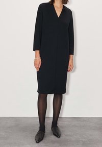 Černé šaty do půli kolen s výstřihem do V a rukávy tři čtvrtiny. Hladký materiál, rovným střihem a nenápadným švem. Spárováno s černými botami.
