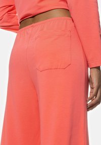 Koralfärgade loungbyxor i mjukt tyg, med elastisk midja, sidoflikar och en enkel bakficka med fyrkantig klaff.