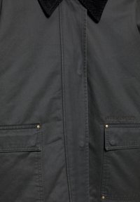 Veste gris foncé avec un col en velours côtelé, deux poches avant à boutons-pression et un détail de logo cousu sur le côté.