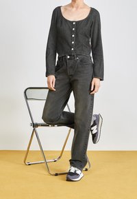 Haut noir en denim à manches longues avec un col arrondi et des boutons métalliques, associé à un jean noir taille haute et des baskets grises avec des accents blancs.
