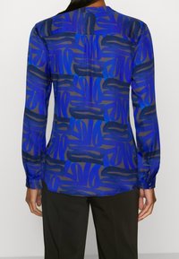 Blue patterned blouse with long sleeves and a neckline. Features an abstract design in darker blue and gray tones; soft fabric texture.