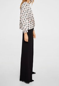 Blouse met een gemusterde ontwerp in roze, zwart en wit, gecombineerd met hoge zwarte broeken. Heeft lange mouwen en een comfortabele pasvorm.