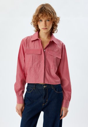 Roodgestreepte cropped shirt met lange mouwen, twee borstzakken en een puntige kraag. Draagt met donkerblauwe denim broek.