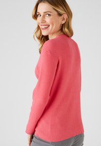 Maglione aderente a coste di un brillante colore rosa, con maniche lunghe e un leggero scollo a V. Texture morbida; la vista dal retro mostra un orlo curvo e una silhouette aderente.