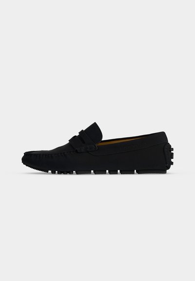 Μαύρο δερμάτινο loafers με λαστιχένια σόλα με μικρές ανωμαλίες και ραφές μοκασίνου σε πλευρική όψη σε λευκό φόντο.