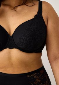 Mustassa pitsissä rintaliivissä on sileät kupit, koristeellinen pitsireunus ja säädettävät olkaimet. Rintaliivissä on saumaton muotoilu ja pehmeä rakenne.